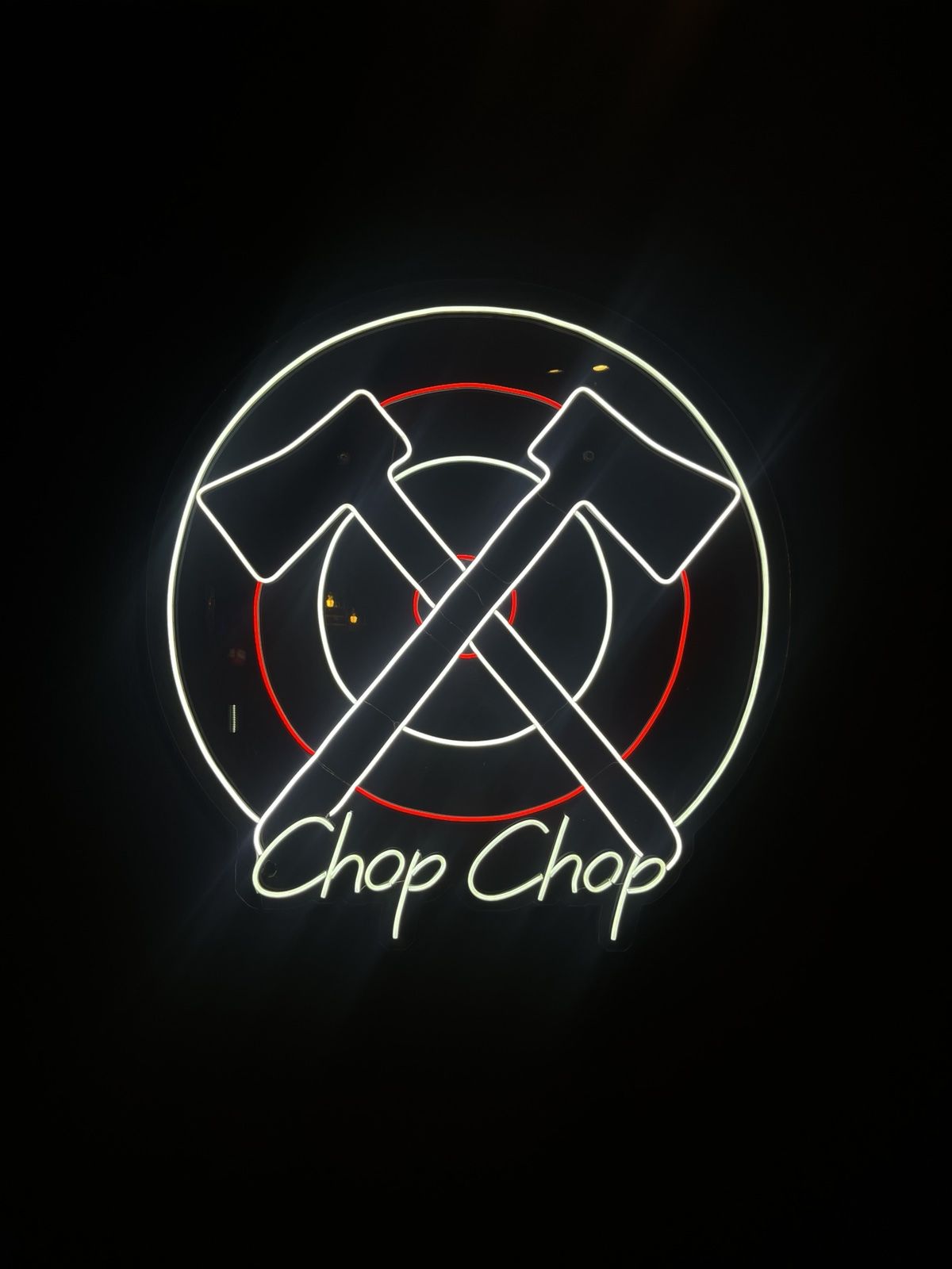 Неонскиот знак на Chop Chop со вкрстени секири врз мета, на црниот ѕид